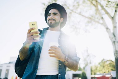 Neşeli, kaygısız İspanyol 'un yaz gezintisi sırasında şık şapkalı akıllı telefonlu, kahveli ve caddeye bakan adamdan.