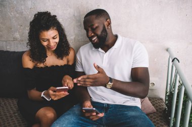 Modern kafede cep telefonlarını karıştırırken gülümseyen gündelik kıyafet giymiş Afro-Amerikan erkek ve bayan arkadaşlarından. 