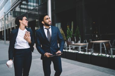 Katı siyah takım elbiseli, gülümseyen çok ırklı iş arkadaşları yazın şehir merkezinde bir binaya bakarak sohbet ediyorlar.