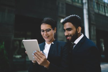 Klasik ofis elbiseleriyle gülümseyen konsantre iş adamları teneffüste şehir merkezinde duruyor ve gündüz vakti birlikte tablet izliyorlar.