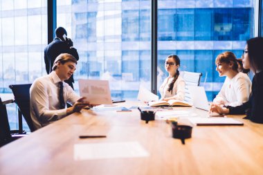 Bir grup başarılı iş adamı konferans masasında oturup pazarlama araştırmalarının sonuçlarını tartışırken, erkek meslektaşları pencerede durup telefonda konuşuyorlar.