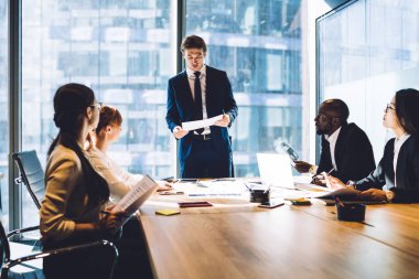 Modern ofiste masa başında oturan çok ırklı erkek ve kadın meslektaşlarıyla yaptığı görüşmede, takım elbiseli bir erkek yönetici konuşuyor. 