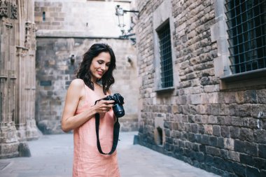 Modası geçmiş şehirde duvarcılık binalarıyla sokakta tek başına dolaşırken elinde fotoğraf makinesi olan genç bir kadının yan görüntüsü. 