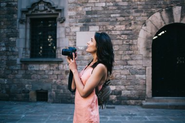 Gayri resmi giyinmiş güzel esmer, eski kasabadaki taş devrinden kalma binanın dış tarafında dikilirken kamera görüntüsü arıyor.