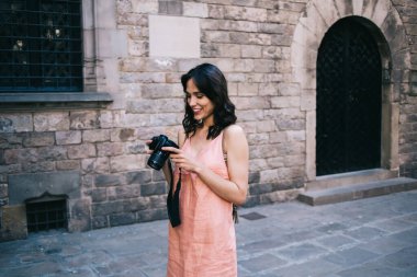 Mutlu, genç bir kadın, gülümseyen ve fotoğraflara bakarken tarihi bir caddede duruyor.