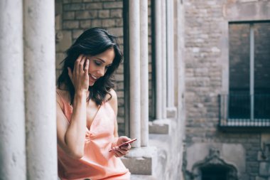 Köşe yazısına yaslanan ve cep telefonuyla sörf yapan mutlu bir kadın. Antik çağlarda telefon ekranında neşeyle saçlarını düzeltiyor.