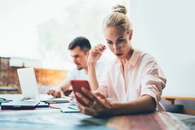 Kendine güvenen, parlak tişörtlü bir kadın. Kafe yaz terasında erkek arkadaşıyla oturuyor. Telefonla ve laptopla çalışıyor.