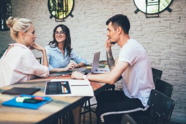 İşbirliği yapan kadın ve erkek, yeni projelerini tartışırken kafeteryada, masada aletler ve programlarla oturuyorlar.