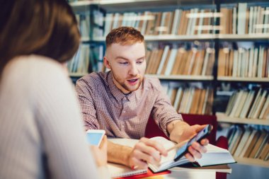 Resmi giyinmiş iş arkadaşları kütüphanenin yanındaki raflarda otururken birbirleriyle faiziyle konuşuyor ve akıllı telefonlar kullanıyorlar.