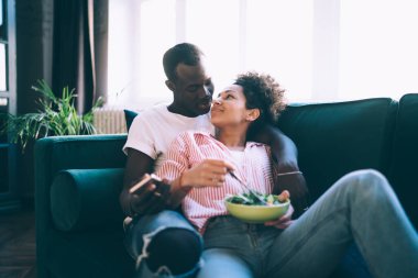 Gündelik aşıklar gibi giyinip birbirine bakarken rahat koltukta salata tabağı ve cep telefonuyla kucaklaşan mutlu insanlar.