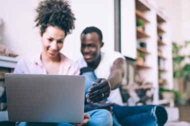 Gülümseyen siyah erkek, gündelik giysiler içinde dizüstü bilgisayarını karıştırıyor. Ekrana bakıyor, pembe tişörtlü, etnik bir kadının yanında oturuyor. 