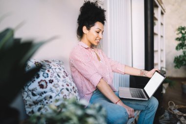 Özenli gülümseyen Afro-Amerikan kadının gündüz vakti modern odada otururken boş ekranla bilgisayarına göz atması.