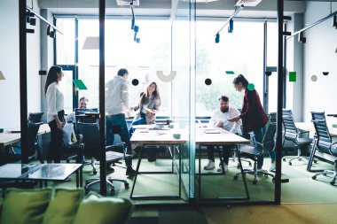Bir grup mutlu iş arkadaşı, modern cam ofis odasının masasında beklerken başarıyı kutluyor ve belgelere bakıyor. 