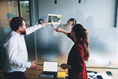 Modern ofis çalışanlarının arka planda durup komşu ofisteki iş arkadaşlarının haritaya işaret ettikleri cam bölme.