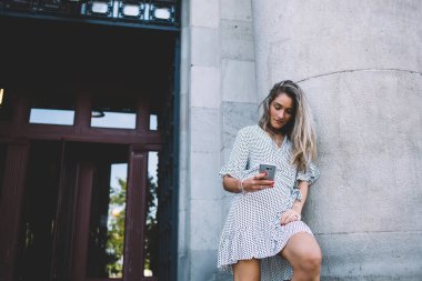 Genç, gülümseyen, uzun saçlı, cep telefonuyla mesajlaşan, yaz günü köşe yazısına yaslanan modern bir bayan.