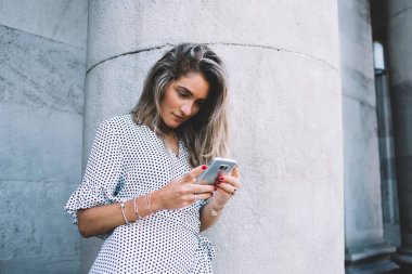 Genç odaklı, puantiyeli, uzun saçlı, cep telefonuyla mesajlaşan yaz günü sokakta sırtüstü uzanan modern bir bayan. 