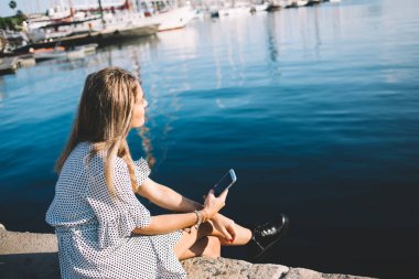 Hayalperest bayanın günlük kıyafetlerini arka planda görmek sosyal medyayı kontrol etmek için telefon kullanarak gezinti güvertesinin bacak bacak üstüne atarak diğer tarafa bakması.