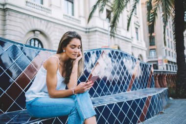 Mimari binalara karşı kenar mahalle dekoratif tezgahına kafa kafaya uzanmış rahatlarken, rahat ve çekici bir kadın cep telefonuna göz atıyor.