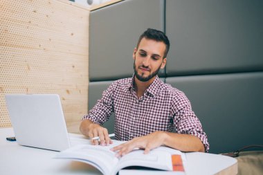 Sakin, gündelik giyinen, kitap okuyan, not defterine not defteri yazan, kafede oturan genç bir adam.