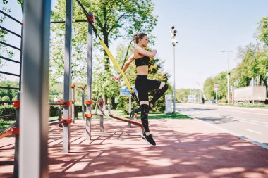 Sıska atletik kadın, sarı saçlı, siyah spor giyimli yazın spor sahasında spor malzemeleriyle atlıyor.