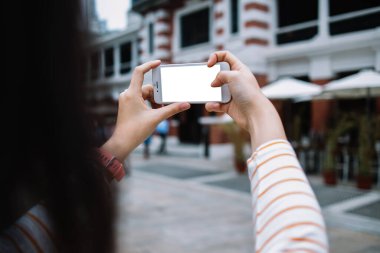 Turuncu çizgili tişörtlü Asyalı bir kadın akıllı telefondan selfie çekiyor ve şehirdeki telefon kamerasından seçim yapıyor.