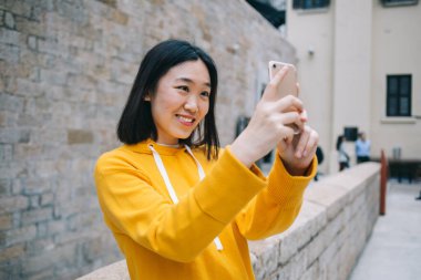 Keyifli modern Asyalı kadın. Günlük giysiler içinde. Akıllı telefonuyla selfie çekiyor.