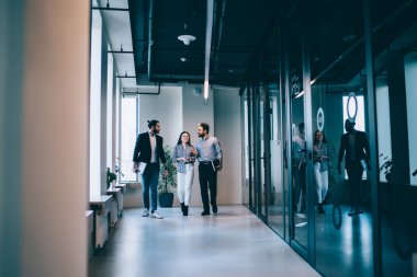 İş toplantısından sonra modern ofis koridorlarında yürürken sonuçları tartışan ve izlenimlerini paylaşan genç profesyonel iş arkadaşları