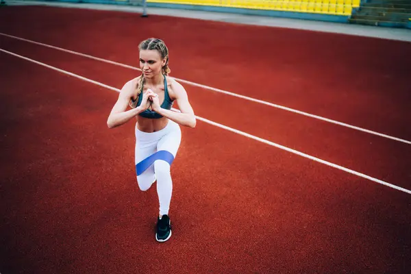 スポーツウェアのアクティブな若い女性はスタジアムでトレーニングし 足にゴム製リボンで肺を吸いながら伸ばします — ストック写真