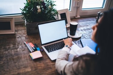 Modern boş dizüstü bilgisayarda internet reklamı için alan alanı olan, kahve dükkanında masada oturan yetenekli bir kadının netbook 'taki içeriği taklit ederken çekilmiş görüntüsü.