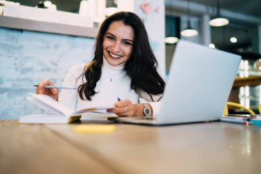 Dizüstü bilgisayar için kameraya bakan 20 'li yaşlardaki neşeli bayan öğrencilerin portresi. Eğitimli mutlu, beyaz bir kadın. Modern netbook teknolojisiyle masaüstünde seviniyor.