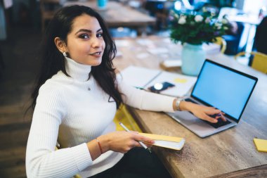 Elinde edebiyat kitabı olan çekici bir kadının portresi çalışma alanında öğrenim görürken kameraya bakıyor, güzel Kafkas milenyumu netbook teknolojisinde uzaktan iş yapıyor.