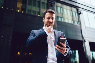 Şehir caddesindeki modern binanın önünde dikilip akıllı telefonlara bakarken takım elbiseli, çene ovuşturan ve gülümseyen mutlu girişimcilerden.