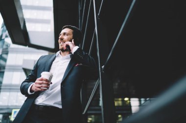 Zarif giyinmiş, akıllı telefon kullanan, işten dinlenen, şehir sokağında kahve içen ve gözlerini başka yöne çevirmiş arkadaşlarıyla konuşan iyimser bir erkek.