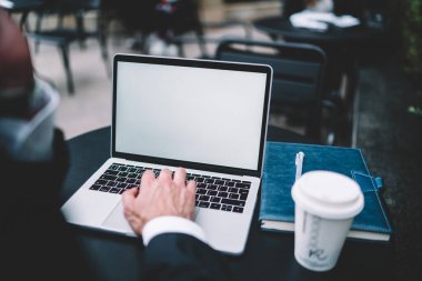 Yukarıdan, takım elbiseli bir iş adamının masadaki tek kullanımlık defter ve kalemle modern dizüstü bilgisayarın klavyesine yazı yazması.