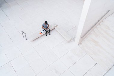 Sokakta mermer avluda elinde belgelerle bankta otururken dizüstü bilgisayar kullanan serbest çalışan bir erkeğin en iyi görüntüsü. 