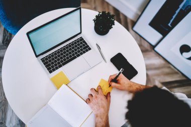 Ofiste dizüstü bilgisayarlı akıllı telefonuyla masada oturan sarı etiketli kalemle notlar alan yüzsüz adamdan.