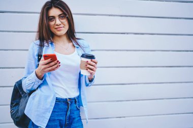 Elinde cep telefonuyla gezip şehir merkezlerinde mesajlar gönderen, promosyon arka planına yakın poz veren güzel bir kadın ve kameraya bakan modaya uygun giyinmiş kadın portresi.