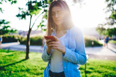 Genç milenyum esmer kadın akıllı telefon çalma listesine yeni şarkı indiriyor. 4G bağlantılarından memnun olan güzel kadın blogcu, aksesuar aracılığıyla müzik dinlerken cep telefonunda multimedya paylaşıyor.