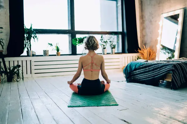 Back view of woman calms brain minds with lotus yoga pose enjoying morning training in home interior with loft design, wellbeing female enjoying free time for meditation for training soul harmony