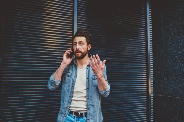 Düşünceli, şaşkın girişimcinin dar görüşlü bakışları, şehir çevresi arasında bulanık mavi çizgili modern bina duvarına karşı caddede dikilirken başka yöne bakması ve telefon etmesi.