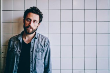 Kendine güveni tam, sırtı sakallı, şık giyinmiş bir adam şehrin arka sokaklarında duvarları olan kameraya bakıyor. 