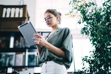 Gözlüklü, tablet üzerinde çalışan zeki bir kız öğrenciden büyük, boş bir kütüphanede dikilirken düşünceli bir şekilde kayıyor.