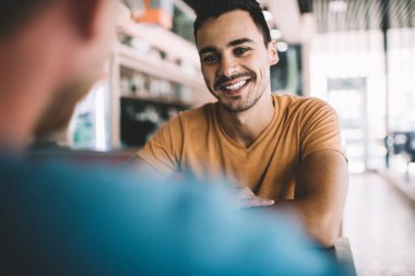 Modern kafeteryadaki toplantı sırasında arkadaşınızla keyifli sohbetler ederken gündelik giysiler içinde mutlu genç bir erkek.