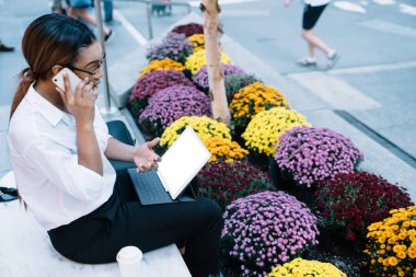 Üzerinde boş ekranlı tabletle Afrikalı Amerikalı yönetici ve akıllı telefon projesini tartışırken şehir caddesindeki çiçeklerin yanındaki bankta oturuyordu.