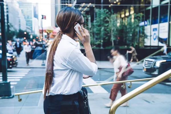 Ofise girerken resmi siyah-beyaz kıyafetler giyen ve cep telefonuyla konuşan, uzun saçlı, modern Afro-Amerikan iş kadını.