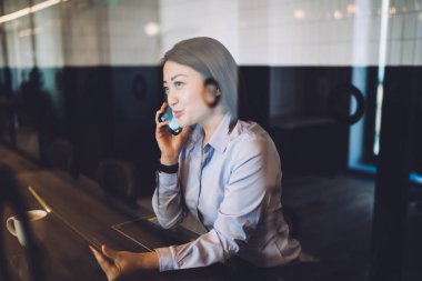 Zarif genç bayan iş kadını akıllı telefondan konuşuyor ve tablet kullanıyor. Bir fincan kahveyle modern kafede oturuyor ve gözlerini kaçırıyor. 