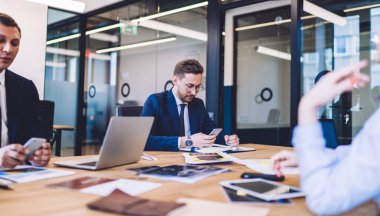 Ofisteki iyi giyimli insanlardan oluşan bir ekip cihazları kullanarak toplantı yapıyor ve belgelerle çalışıyor. Cep telefonlarında geziniyor ve mesajlaşıyor.