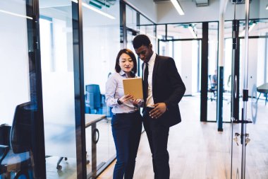 Resmi olarak çok ırklı genç bir çift, şirket bürosunun koridorunda ayakta duran bir kadın tarafından el ele tutuşurken tarayıcı tablet giyerler. 
