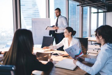 Şık resmi gömleklerle konsantre olmuş meslektaşlar, modern ofisin masasında açık kentsel altyapı üzerine tablet kullanırken doküman okuyorlar.