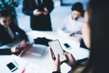 Yukarıdan gelen ve boş ekranlı cep telefonu kullanan bir kadın, açık ofisteki iş arkadaşlarıyla toplantıda.